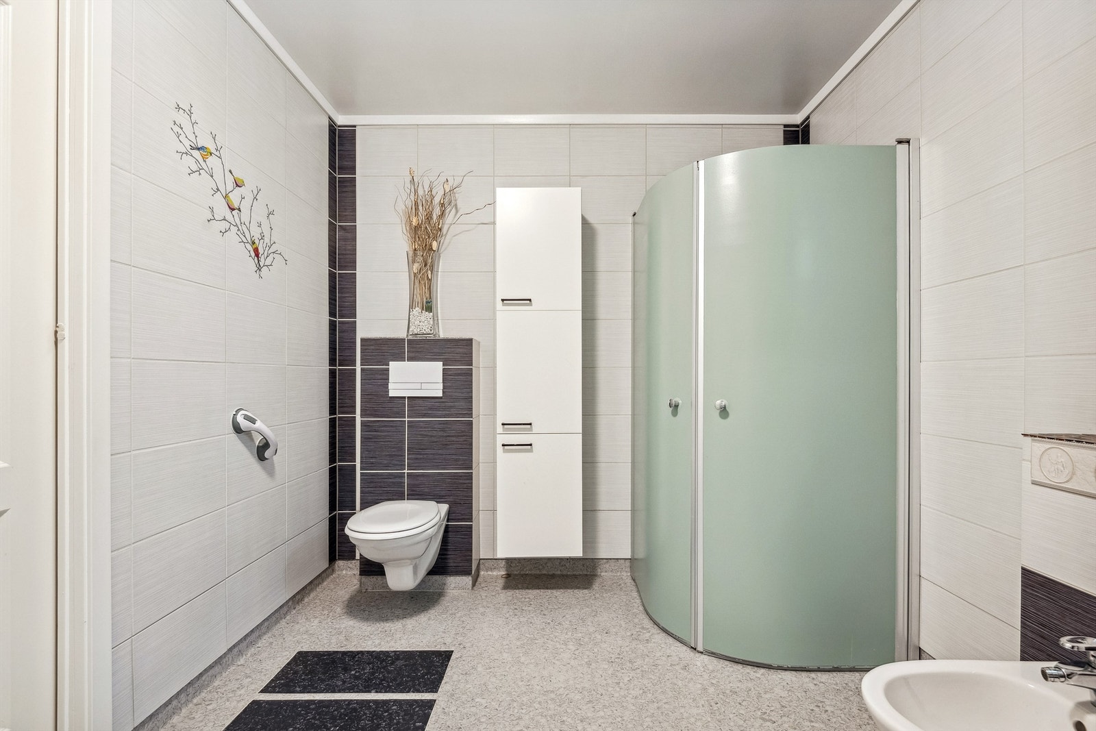 Veggmontert toalett, bidet, samt dusjvegger i et hjørne. Det er også opplegg for vaskemaskin. Galleribilde