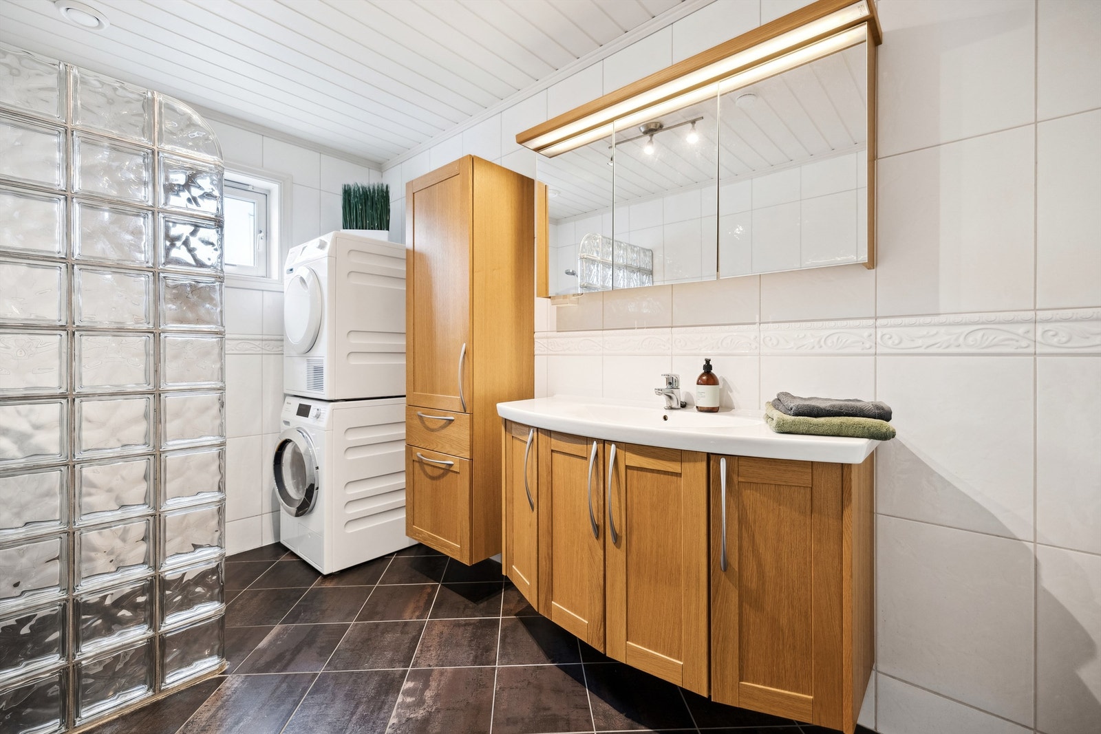 Det flislagte badet ble pusset opp i 2007 og har en romslig baderomsinnredning i eikeutførelse, opplegg til vaskemaskin og tørketrommel samt dusjhjørne med vegg i glassbyggerstein Galleribilde