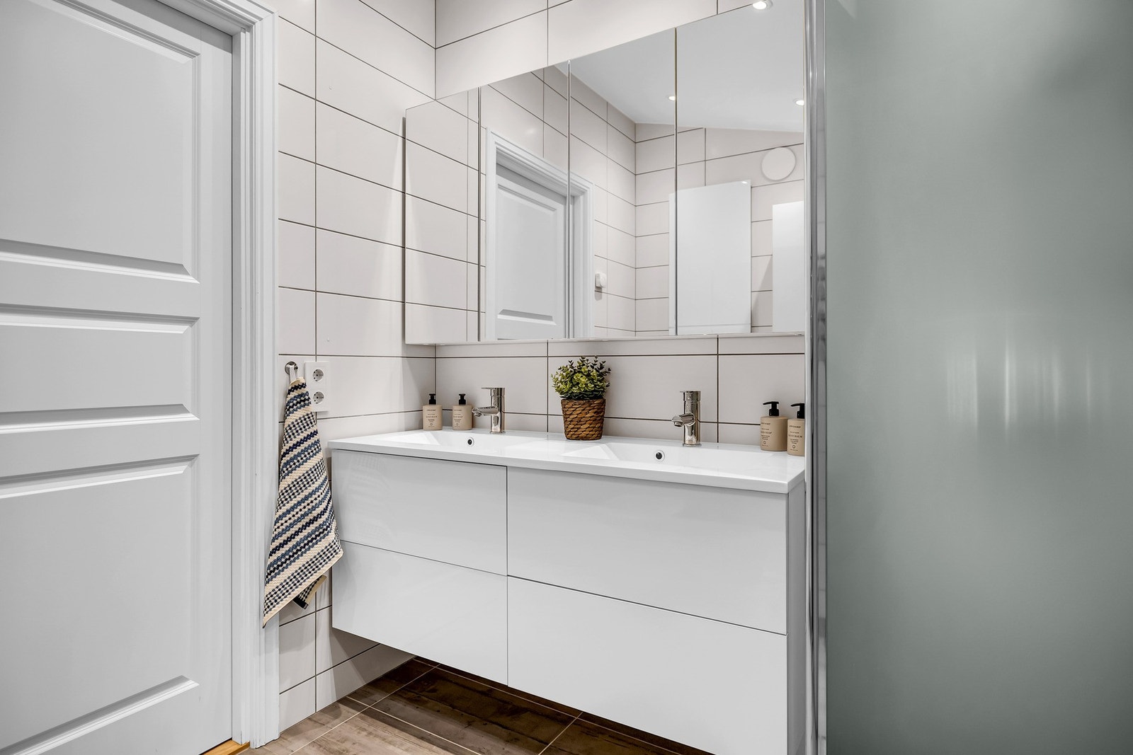 Videre er det dusj på gulv med innfellbare glassdører tilkoblet veggmontert hånd- og regndusj og vegghengt toalett. Badet har opplegg for vaskemaskin og tørketrommel. Galleribilde