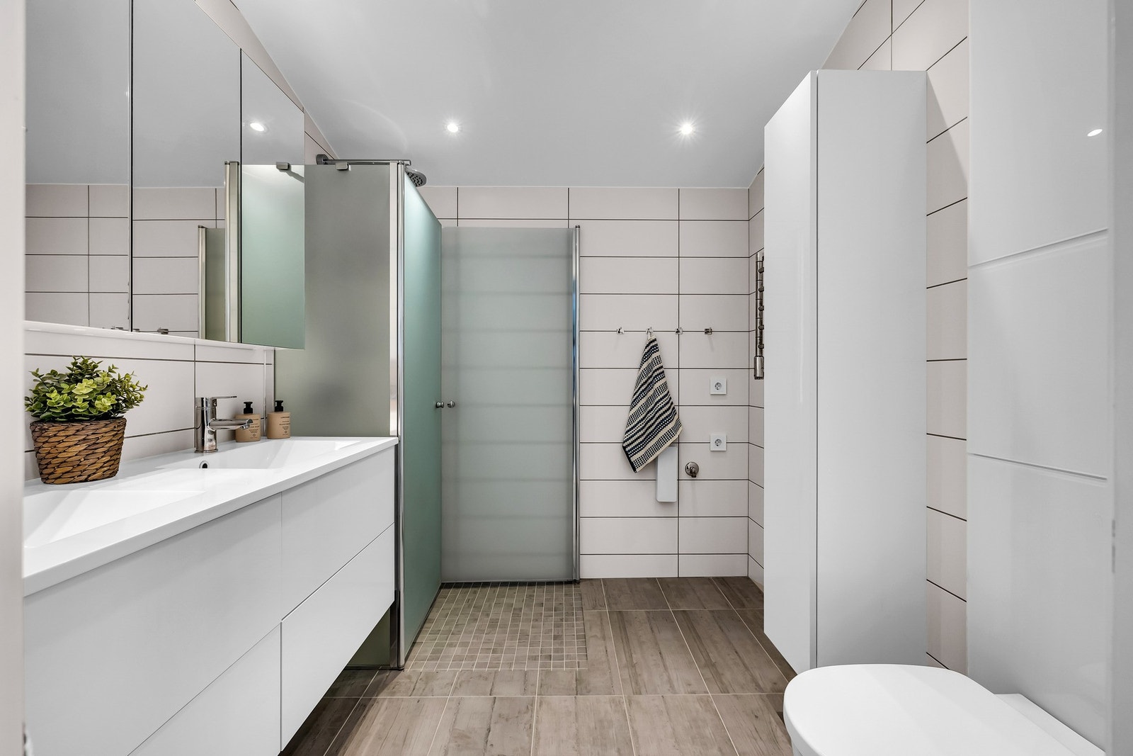 Baderommet er fra byggeåret 2016 i tidløs utførelse med flislagte overflater og varme på gulv. Badet er utstyrt med vegghengt servantskap med dører, dobbel servant og speilskap. Galleribilde