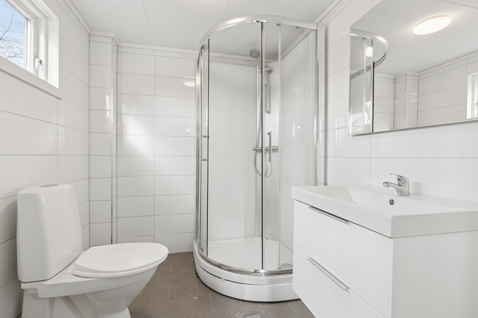 Flislagt bad/wc med varmekabler i gulv, vegghengt servant, speil og dusjkabinett. Galleribilde