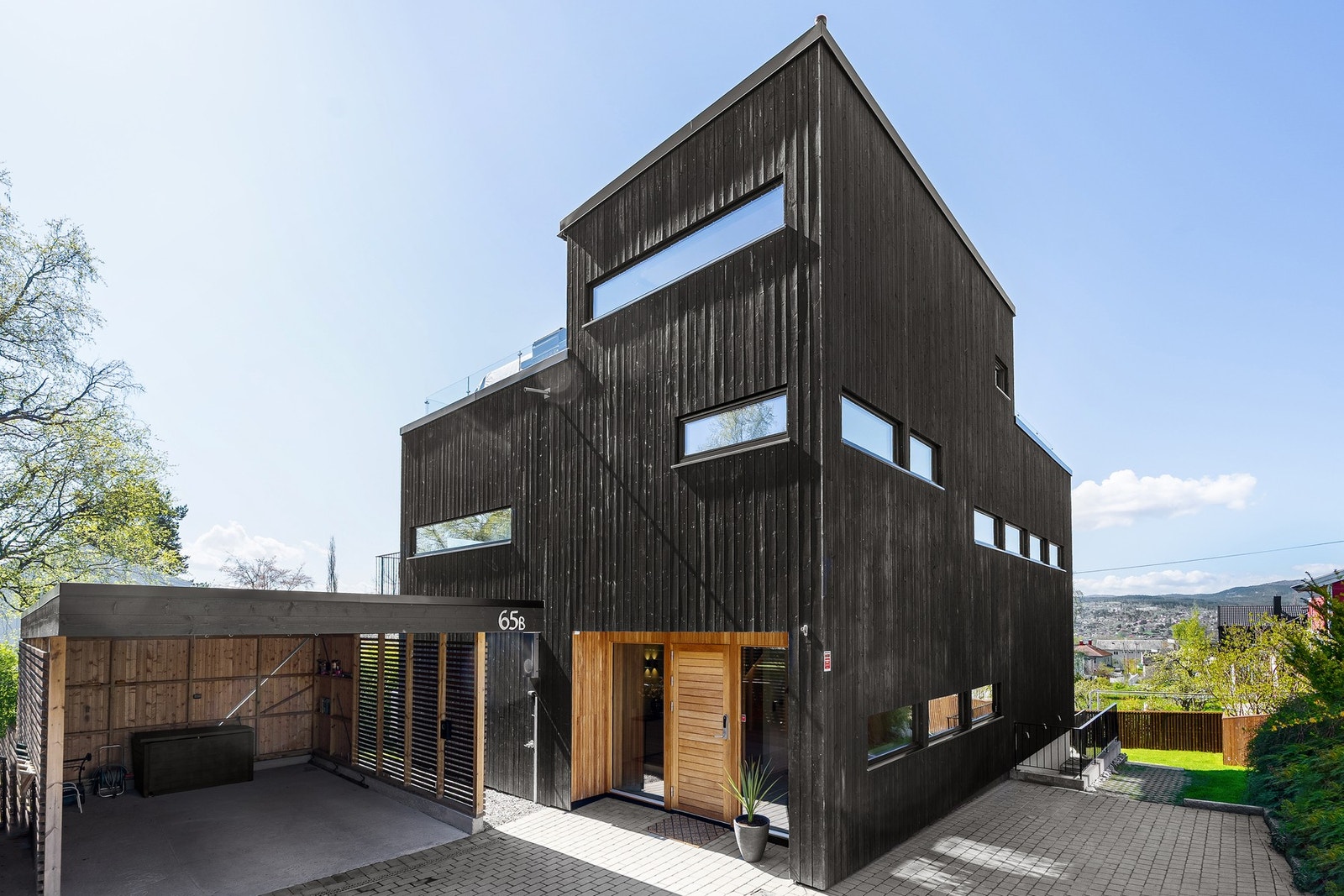 Stilren funkisbolig over fire etasjer med sort trekledning, store vindusflater og moderne uttrykk. Boligen har carport, takterrasse og nydelig utsikt. Galleribilde