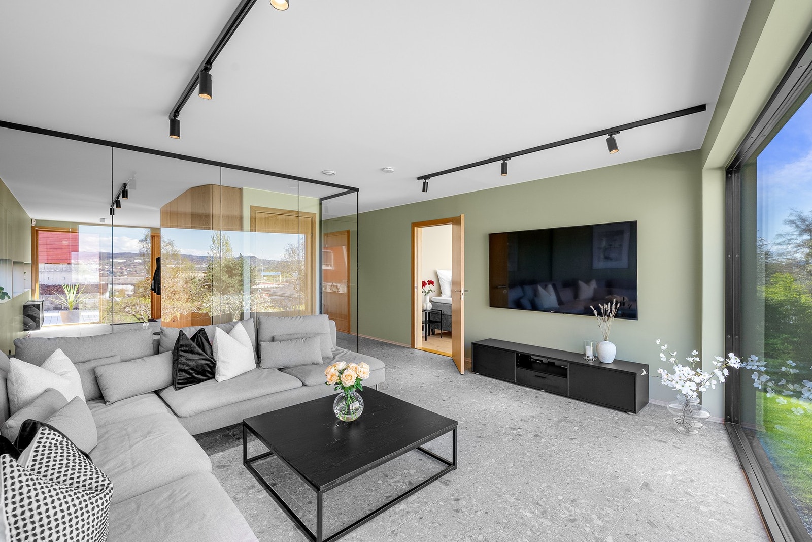 Lunt og stilrent oppholdsrom med grønnfargede vegger, terrazzo-inspirert gulv og moderne glassvegg mot entré - praktisk plassert nært soverommene. Galleribilde