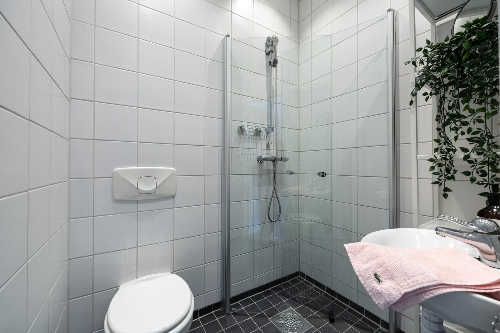 Badet er innredet med vegghengt servant med ett-greps armatur, vegghengt speil over servant, dusjhjørne med innfellbare glassdører og dusjarmatur tilkoblet hånddusj, samt vegghengt toalett tilkoblet sisternekasse. Galleribilde