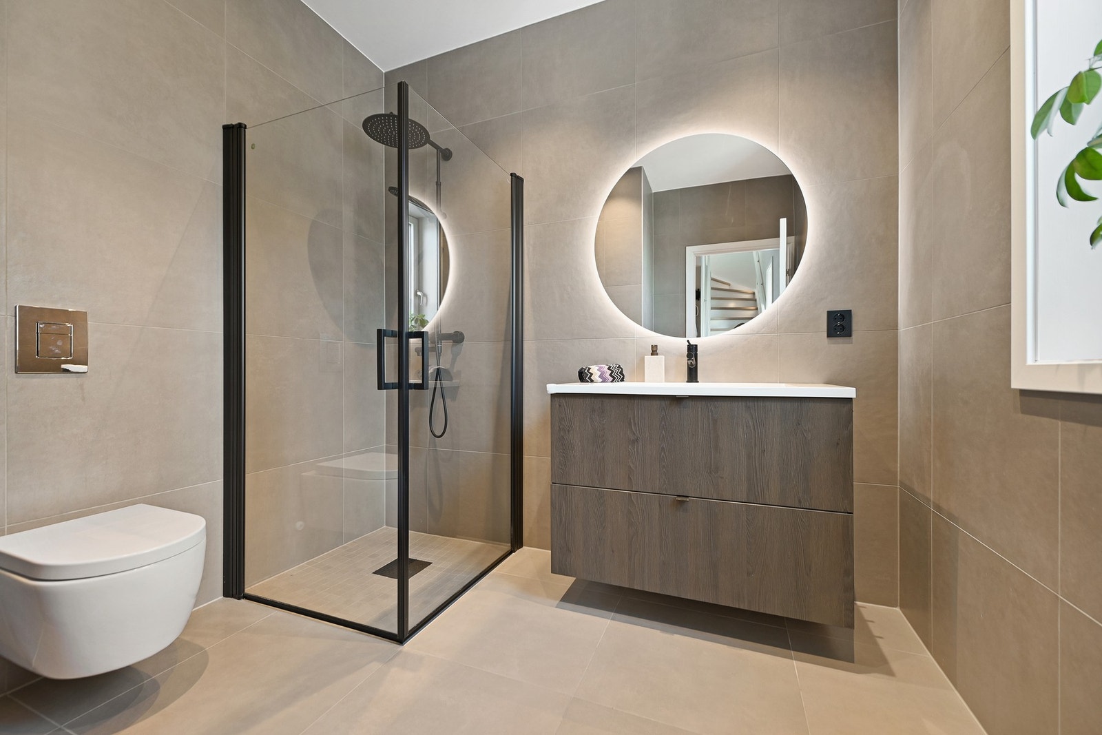Badet byr på en romslig følelse med sine rene linjer og moderne materialvalg. Flislagte overflater i nøytrale farger gir et tidløst uttrykk, og sammen med godt plasserte lyskilder, sørger dette for lyse og innbydende rom. Badet er oppgradert fra standardl Galleribilde