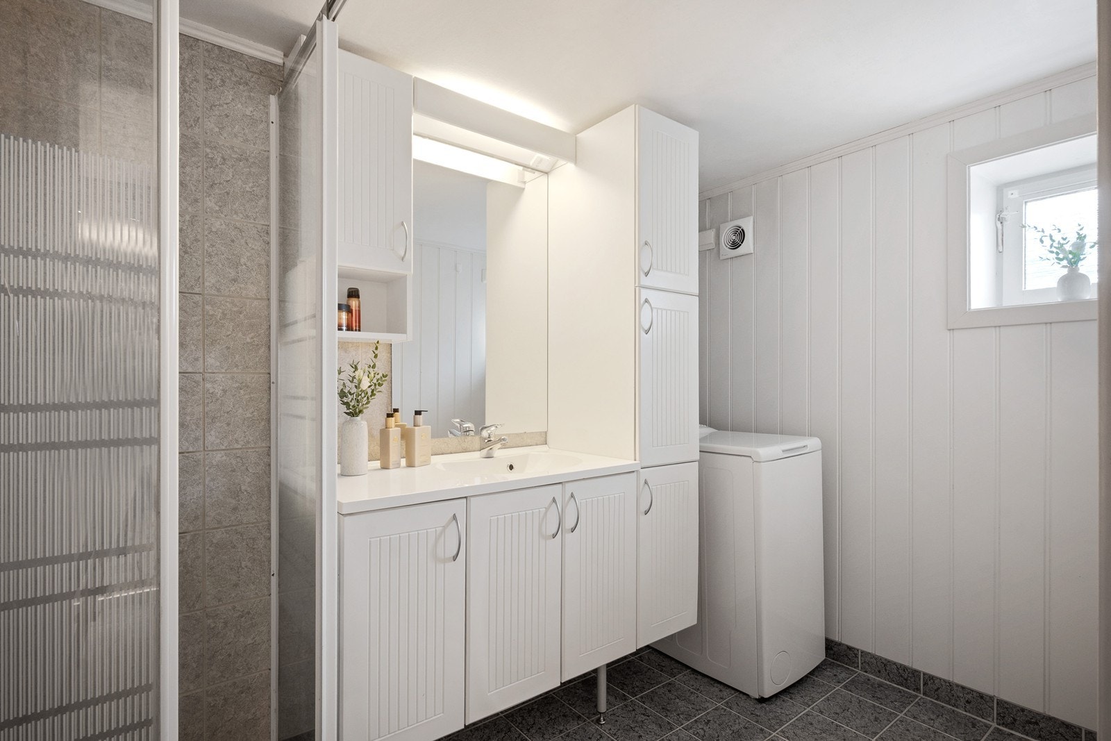 Badet har flislagt gulv med varmekabler, godt med oppbevaring i servantskap og røropplegg for vaskemaskin. Galleribilde