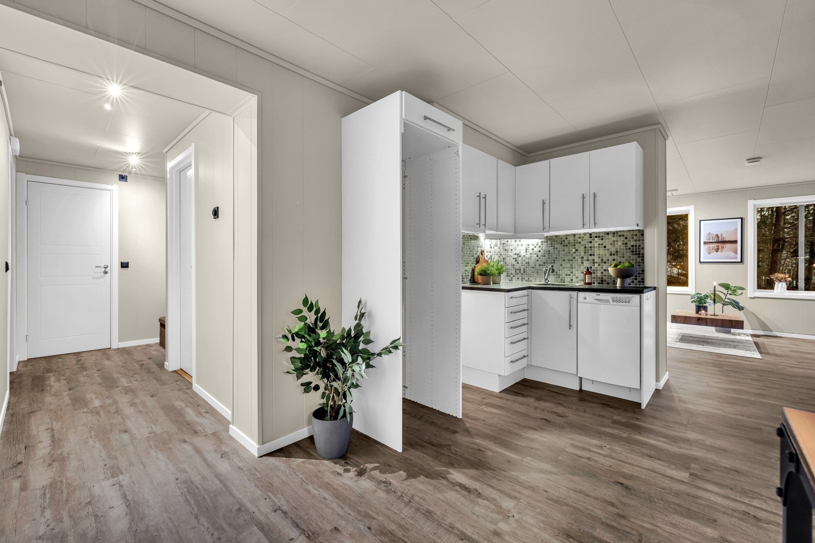 Kjøkkenet er fint plassert i midten av leiligheten. Stilrent kjøkken i åpen løsning mot stuen, fra 2007. Kjøkkeninnredning med hvite fronter og håndtak. Avsatt plass til hvitevarer. Oppvaskmaskin medfølger Galleribilde