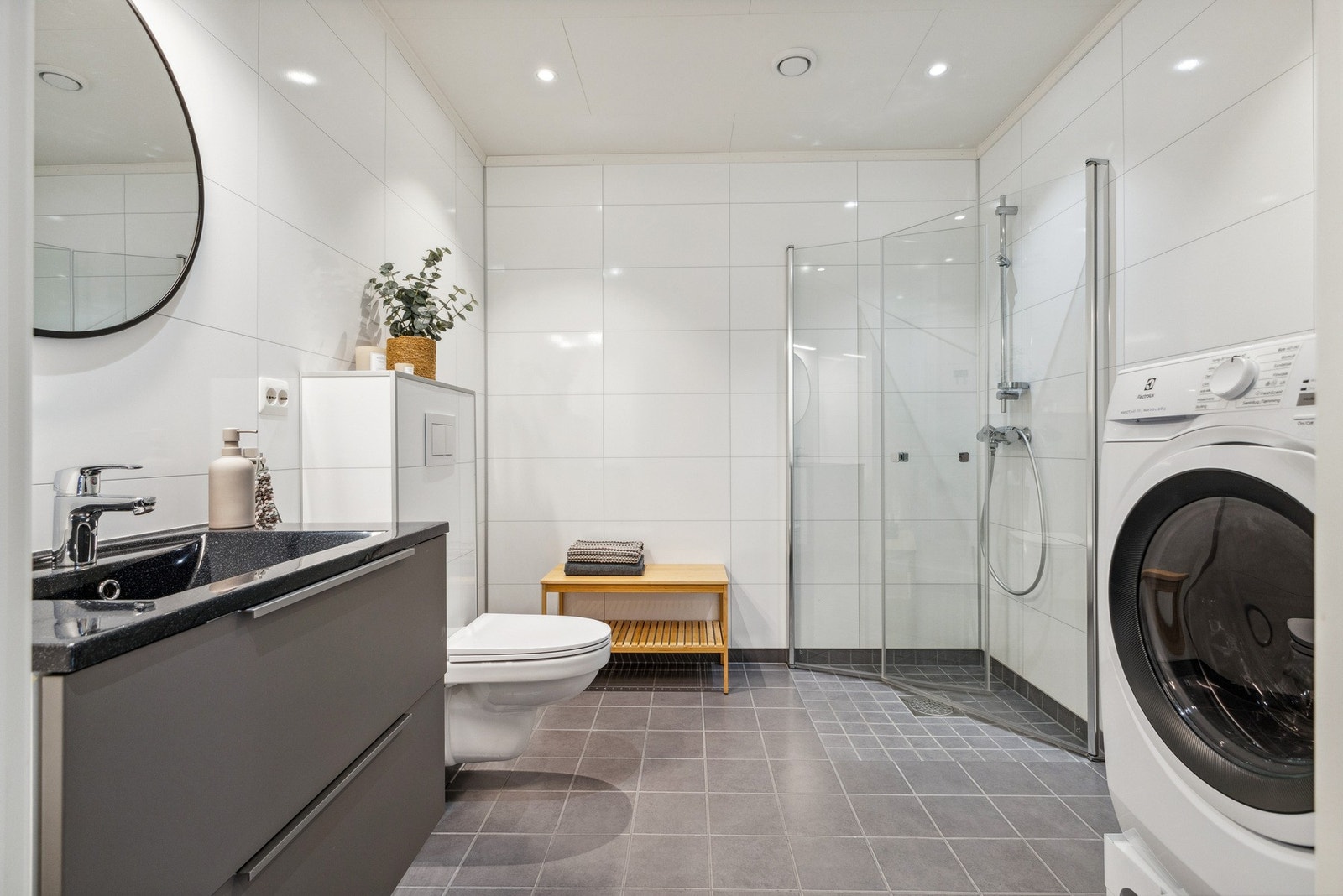 Leiligheten har 2 bad - en praktisk løsning for både familier og besøk. Dette badet er stilrent og behagelig. Her får du dusjhjørne, toalett, godt med lys og opplegg for vaskemaskin. Galleribilde