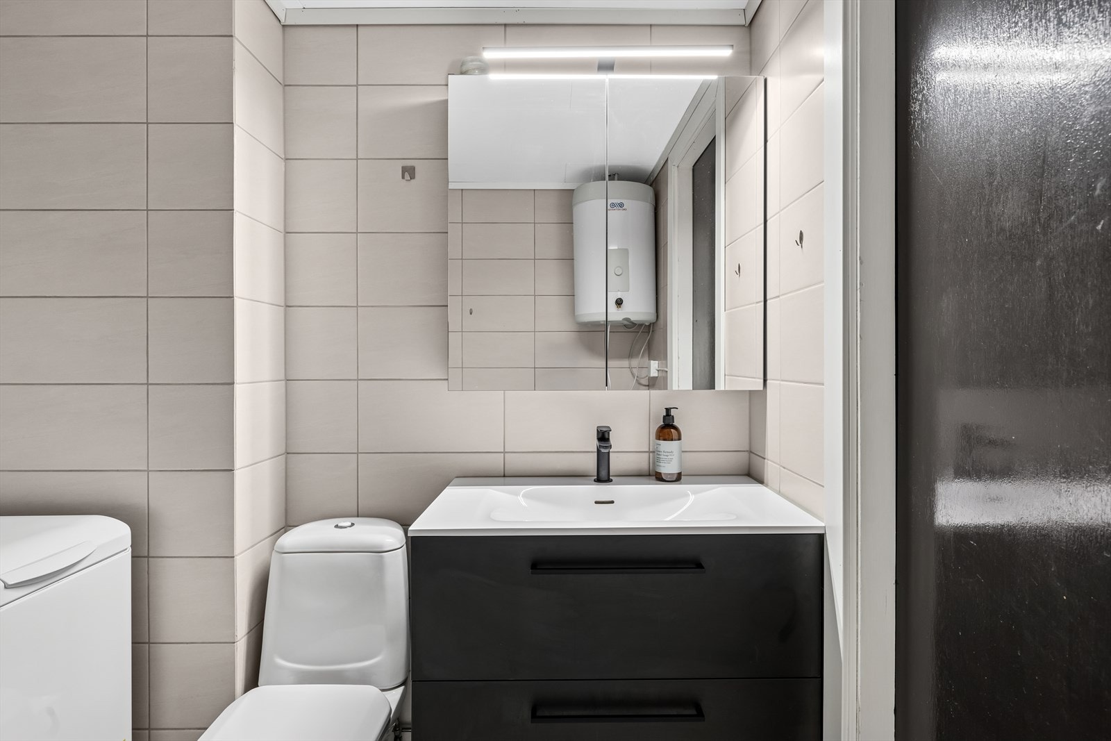 Badet inneholder gulvstående toalett, innredning, speilskap, opplegg for vaskemaskin og dusjkabinett. Galleribilde