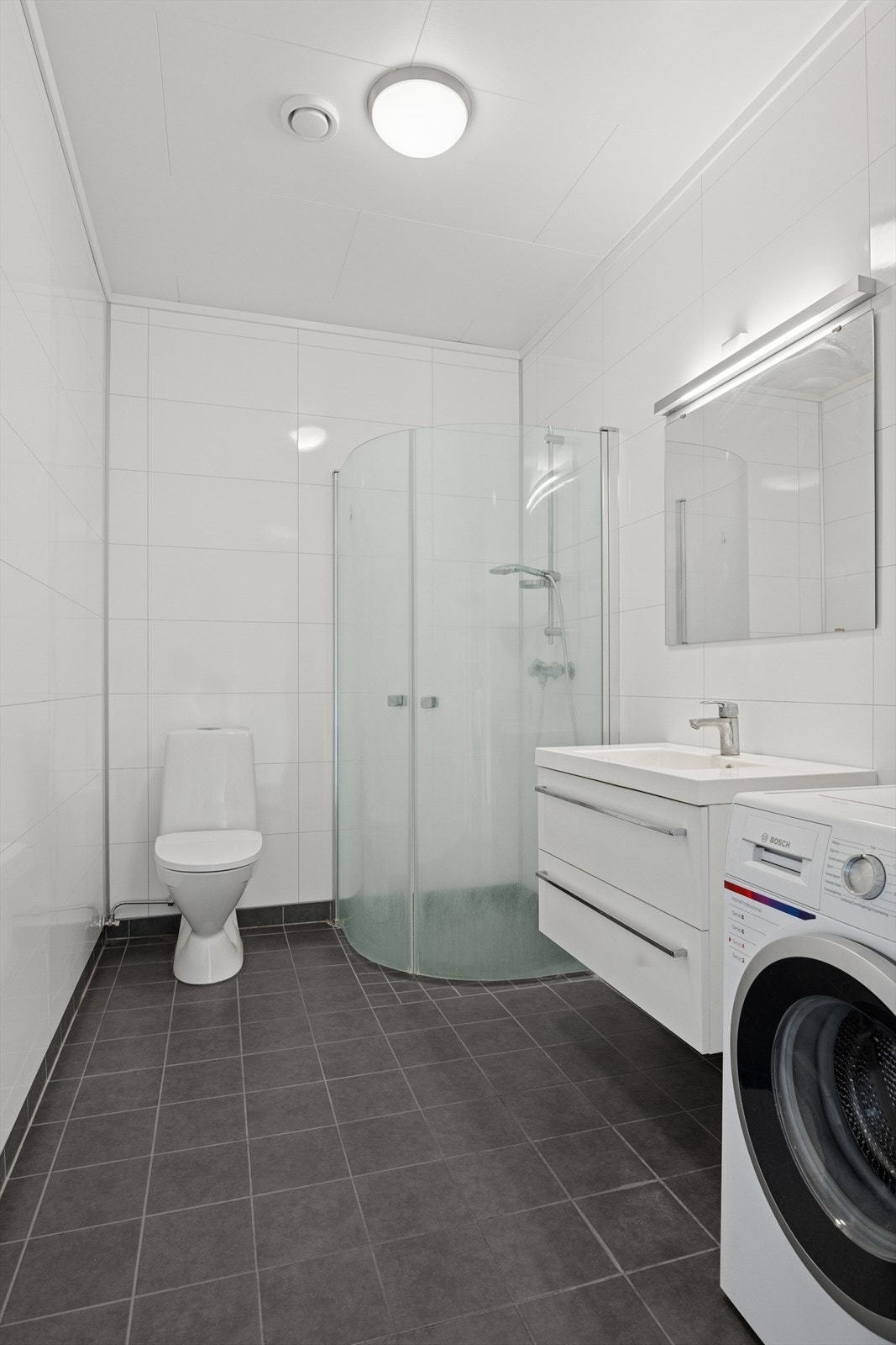 Leilighetens bad er romslig med opplegg for vaskemaskin. Badet har våtromsplater på vegg og fliser på gulv. Galleribilde