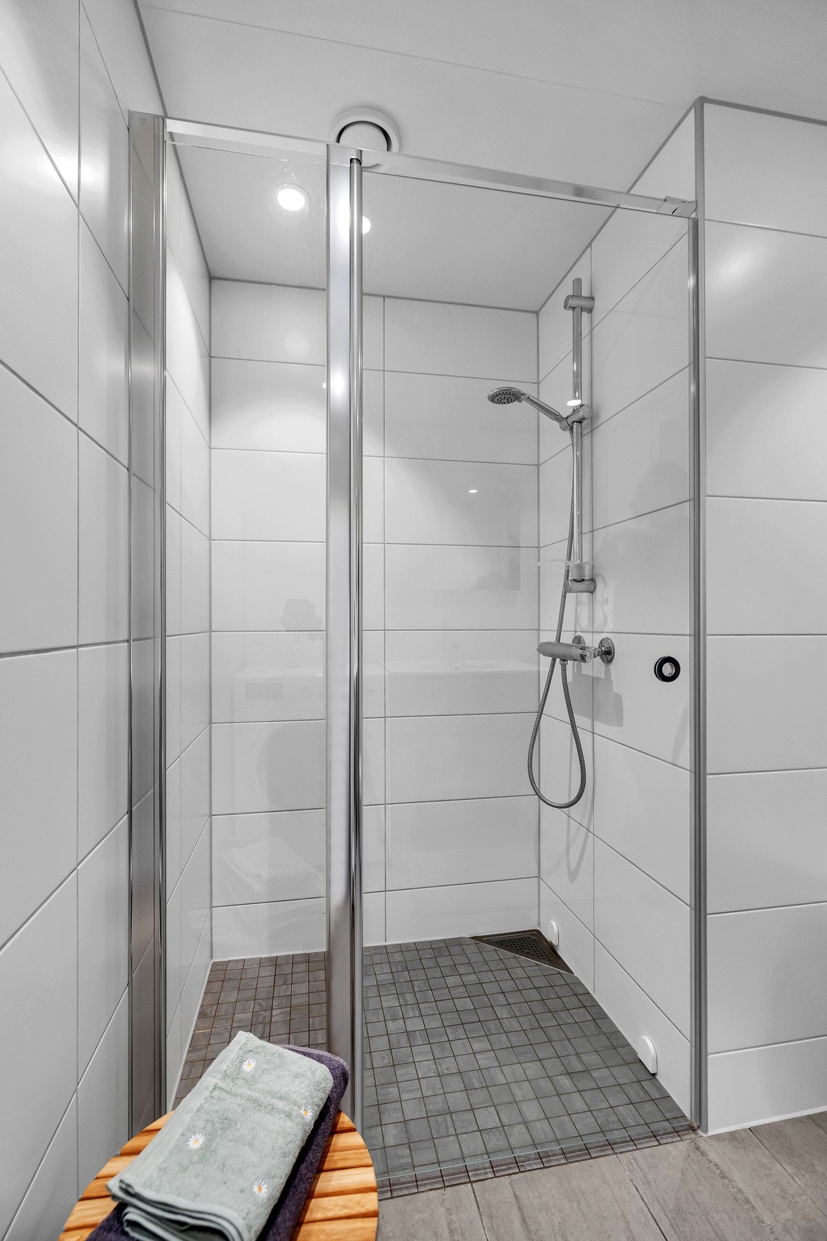 Badet består av vegghengt toalett, servant på vegghengt servantskap, vegghengte dusjdører i glass og speil med integrert belysning. Galleribilde