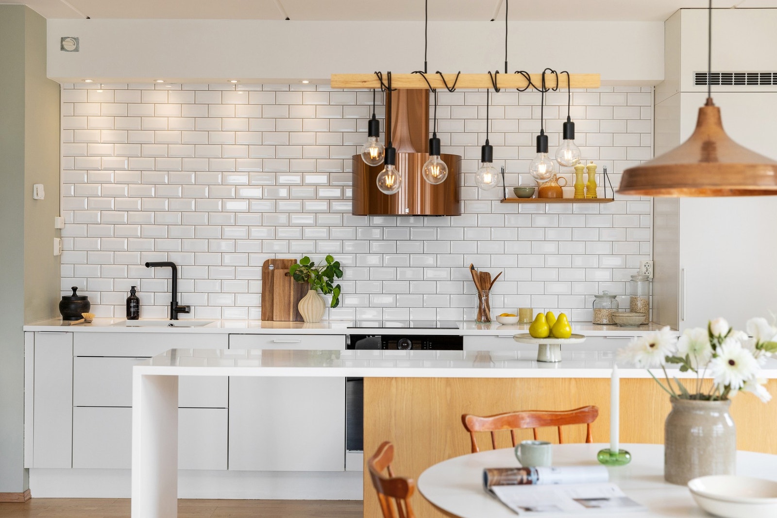 Benkeplaten er i helstøpt Corian, som gir en sømløs og eksklusiv finish. Langs benkeryggen er det lagt fliser i et stilrent design, og kjøkken ventilatoren er valgt i en delikat farge som harmonerer med resten av innredningen. Galleribilde