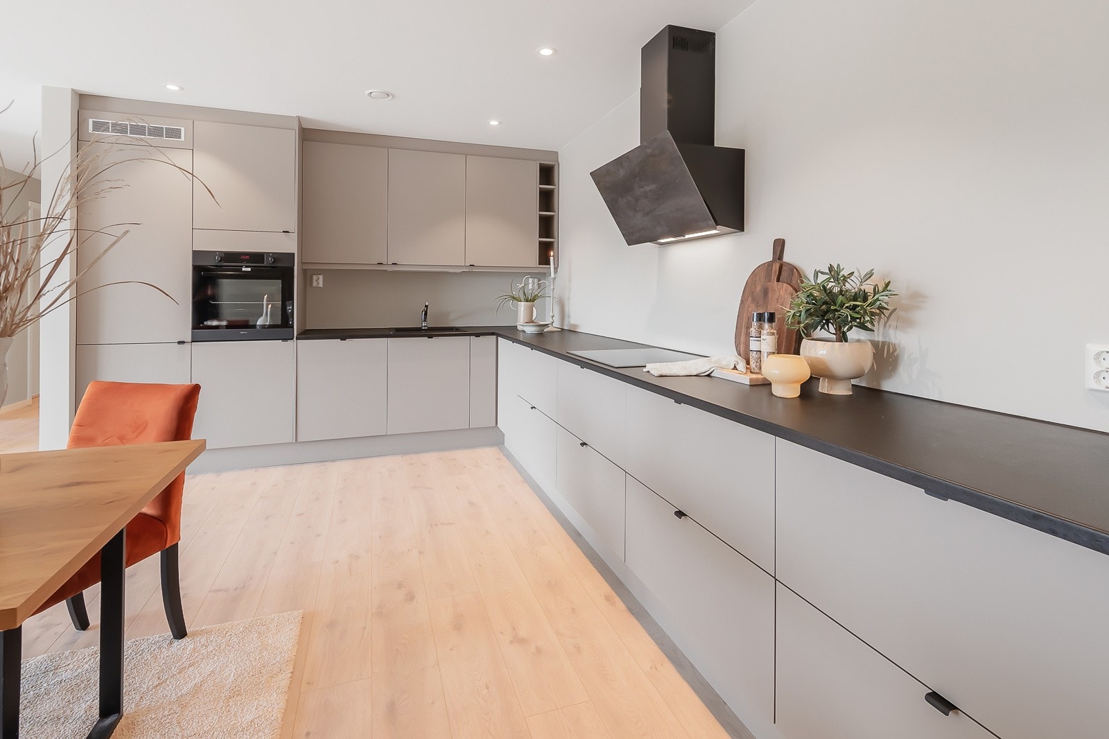 Utvidet kjøkken med ekstra skap og benkeplass. Leverandør Systemnkjøkken. Det er innebygget kjøleskap/stekeovn/oppvaskmaskin og platetopp. Dekorativ ventilator på vegg. Galleribilde