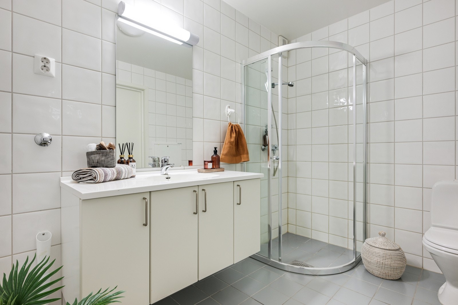 Lekkert baderom med hvite fliser på vegg og mørk flis på gulv. Her kan man dusje i et dusjhjørne med nye dusjvegger fra 2024 Galleribilde