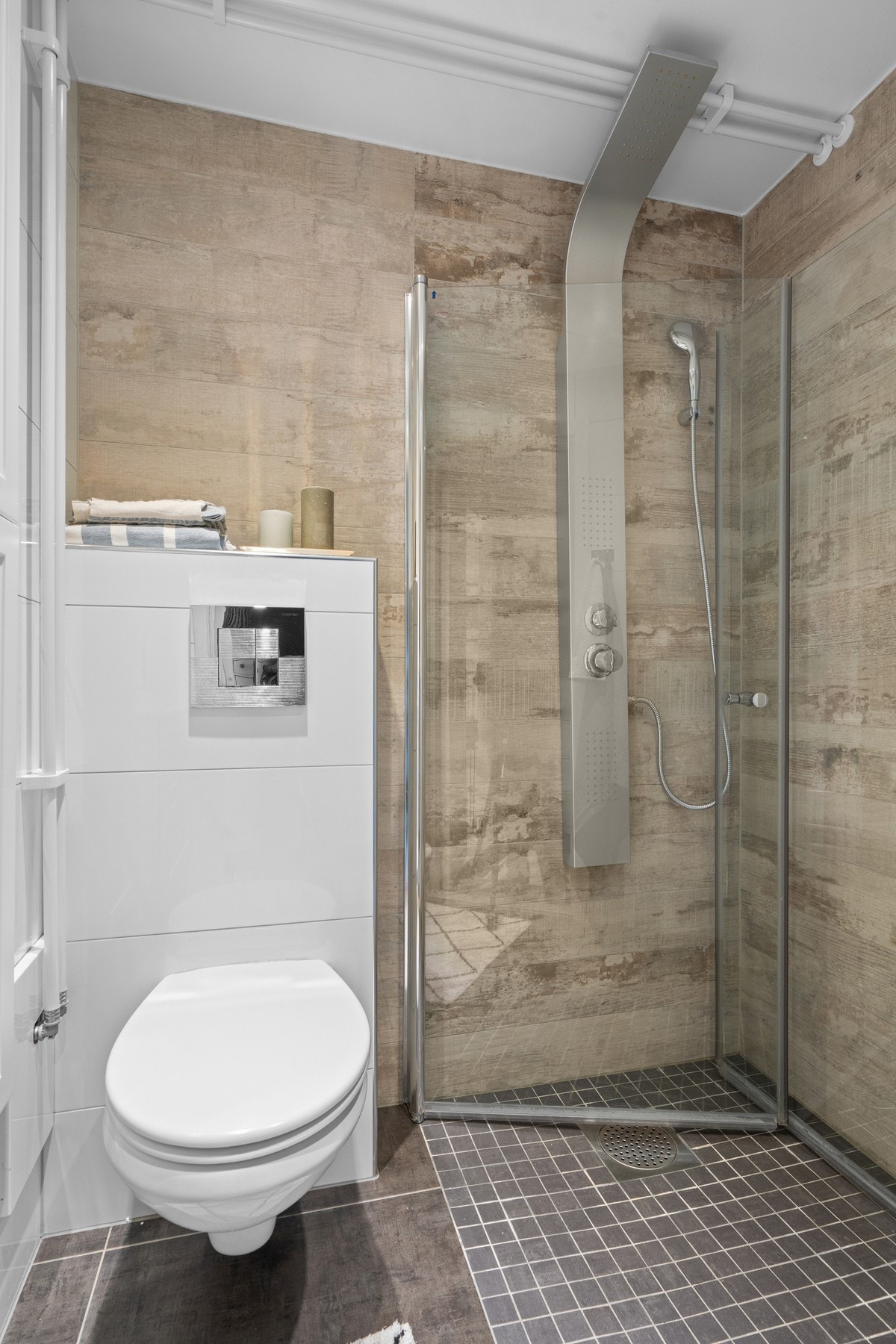 Badet er utstyrt med dusjhjørne med innfellbare glassdører, vegghengt toalett, servantskap med ettgreps blandebatteri og speil med belysning. Galleribilde