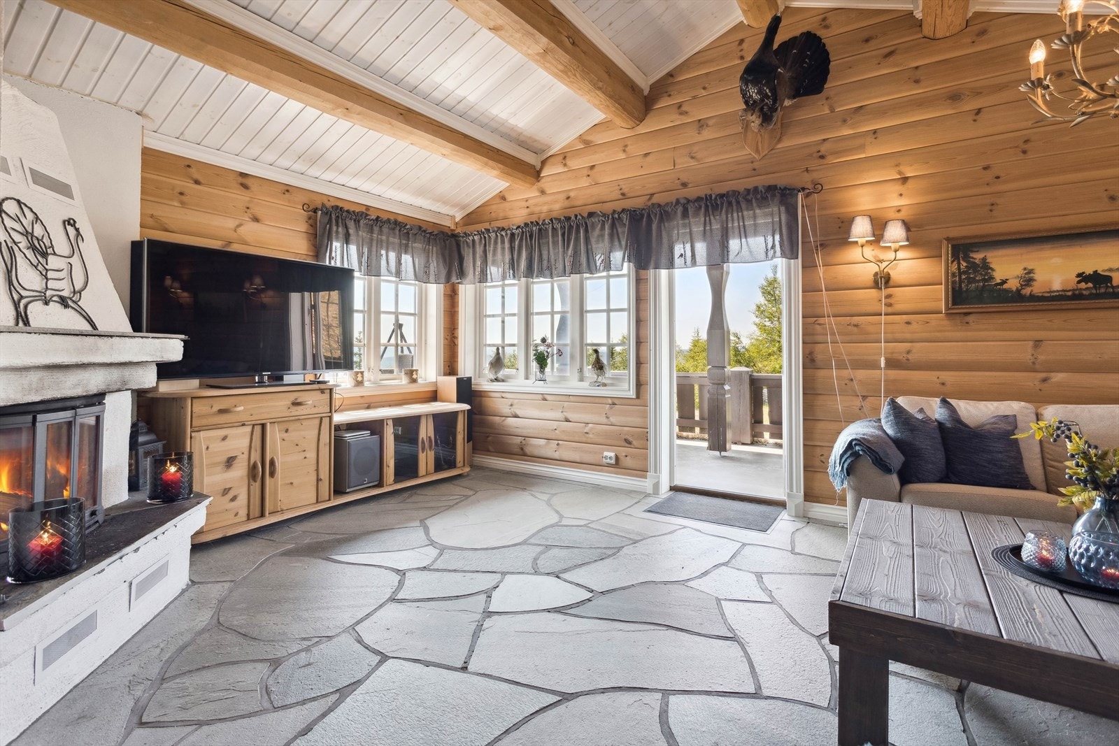 I 1. etasje har du en lys og hyggelig stue med steinfliser på gulv med gulvvarme, overflater med panel og mønet himling med lysmalt panel og synlige rundstokker. Galleribilde