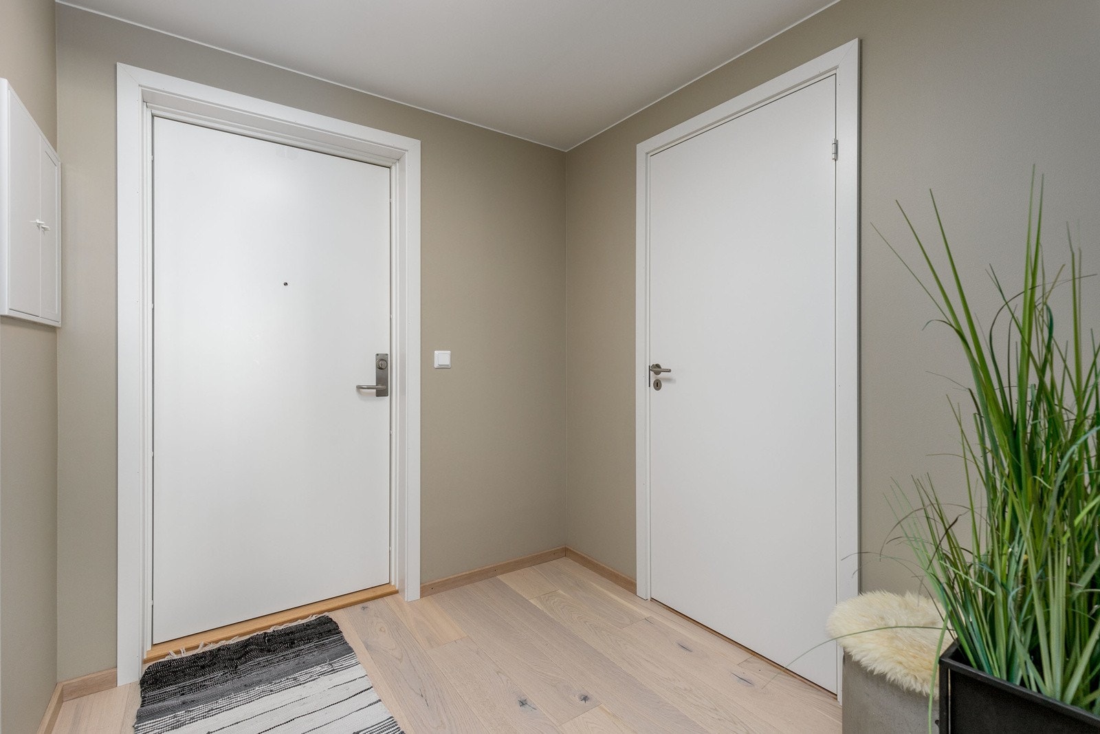 Tiltalende entre/gang med lekker hvitpigmentert parkett på gulv og lysmalte veggflater som gir et godt førsteinntrykk av leiligheten Galleribilde