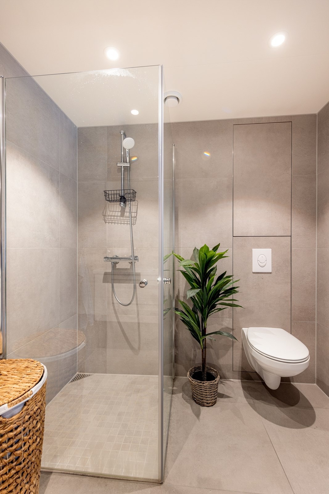 Romslig, vegghengt baderomsmøblement med praktiske underskuffer, heldekkende servantplate og veggmontert speilskap og belysning over vask. Praktisk dusjhjørne med innfellbare dusjdører og veggmontert toalett. Galleribilde