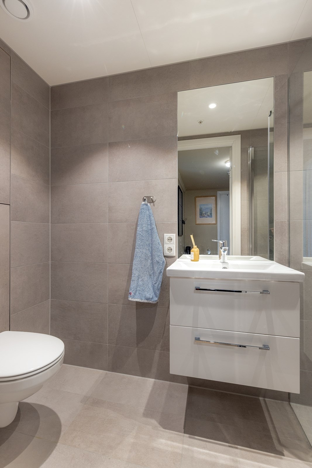 Praktisk, vegghengt baderomsmøblement med dype underskuffer, heldekkende servantplate, speil og belysning over vask. Fin dusjnisje og vegghengt toalett. Galleribilde