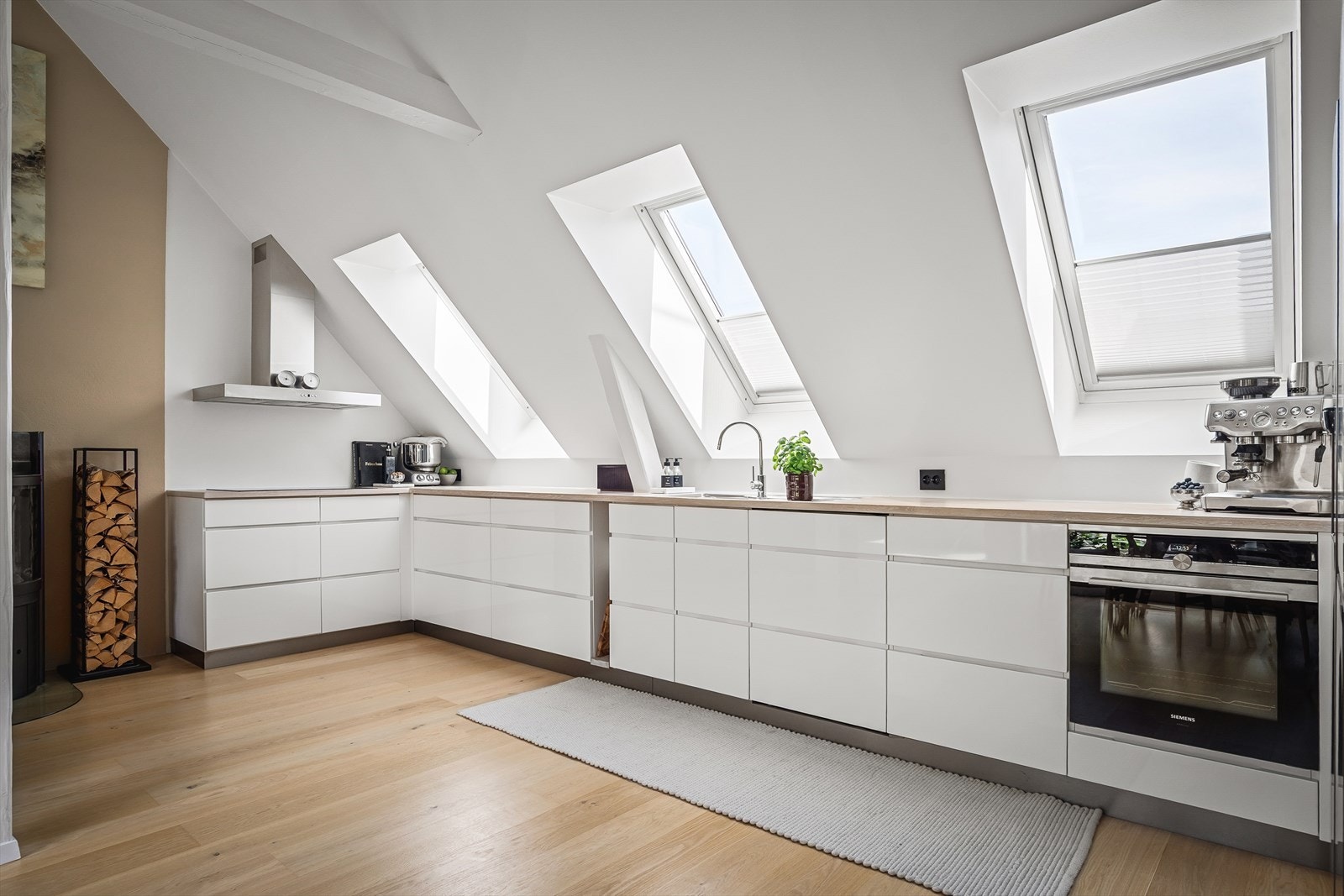 Lys og moderne kjøkkeninnredning fra KVIK. Kjøkkeninnredningen består av glatte fronter og benkeplate i treverk med nedsenket kum i rustfritt stål. Galleribilde