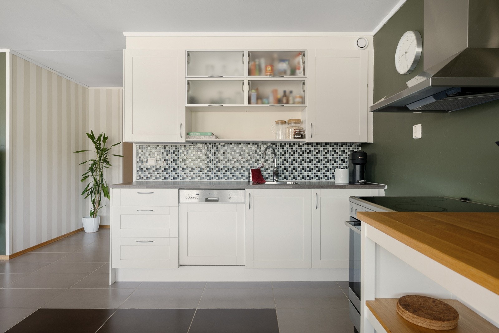 Kjøkkenet har innredning med hvite, profilerte fronter. Noen av overskapene har fronter med frostet glass. Benkeplaten er i laminat med nedfelt stålkum. Galleribilde