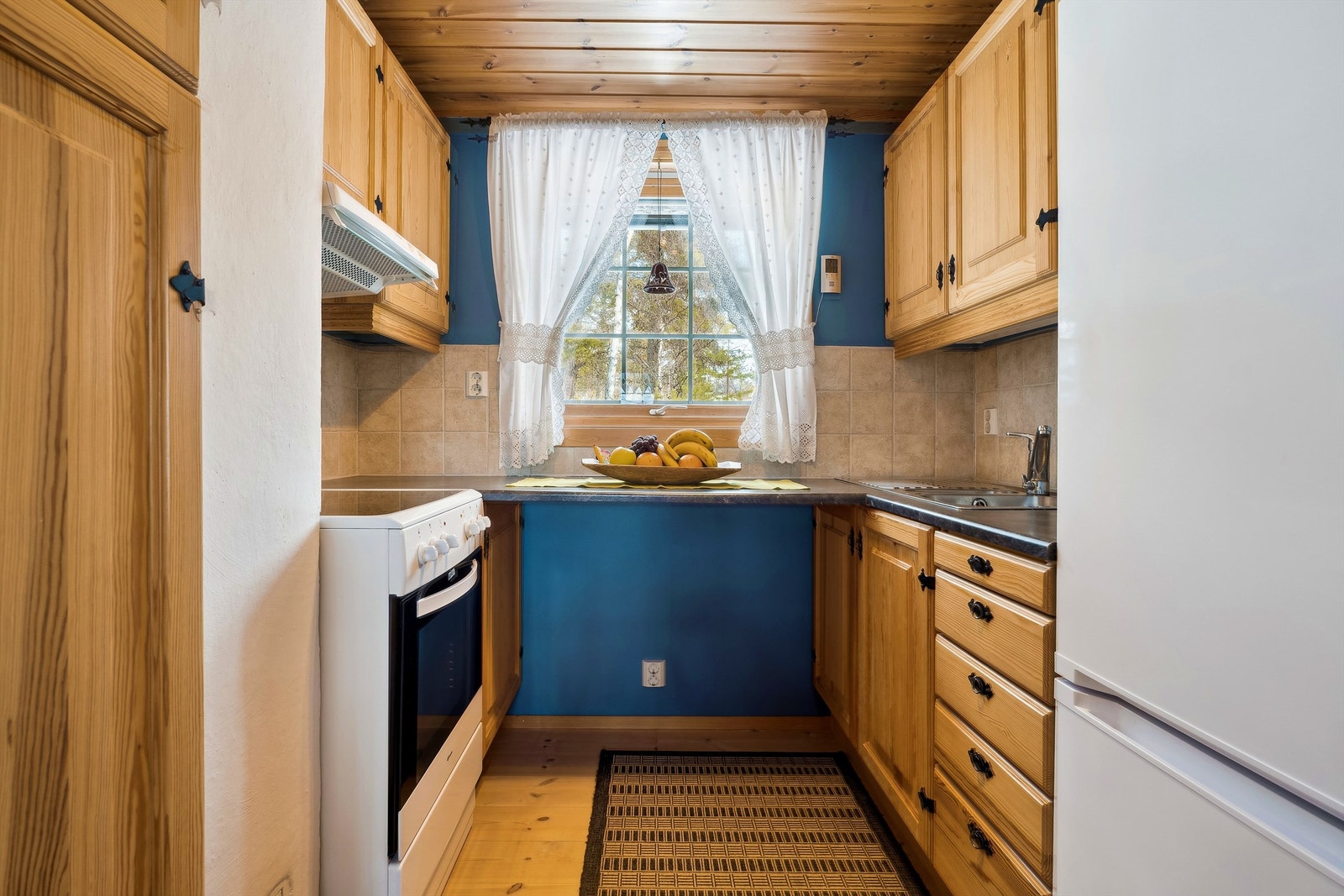 Heltre kjøkkeninnredning med profilerte, lakkerte furufronter. Laminert benkeplate med nedfelt kum. Galleribilde