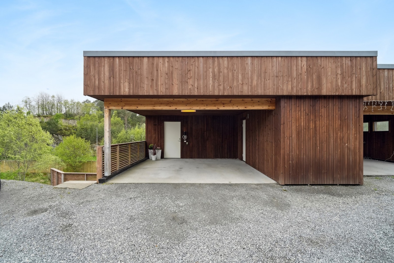 Praktisk integrert carport ved inngangspartiet, med en tilhørende romslig bod som gir godt med lagringsplass. Galleribilde