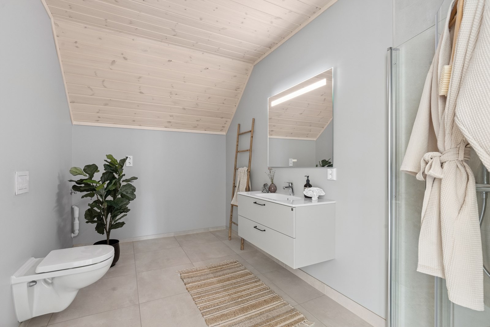 Badet i andre etasje har malte vegger utenom i dusjnisjen som har fliser. Av sanitærutstyr har badet vegghengt toalett fra Villeroy & Boch, baderomsinnredning med speil med lys fra Drømmekjøkkenet. Galleribilde