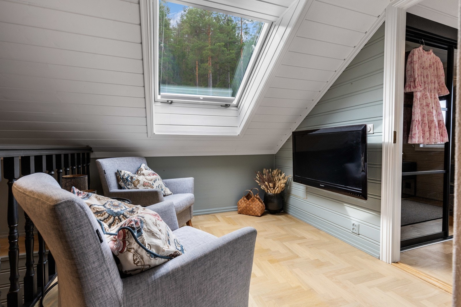 Stuen er holdt i en moderne stil med parkettgulv, harmonisk farge på veggpanel, mørkmalt gelender mot trappen og skråhimlingen med takvindu. Galleribilde