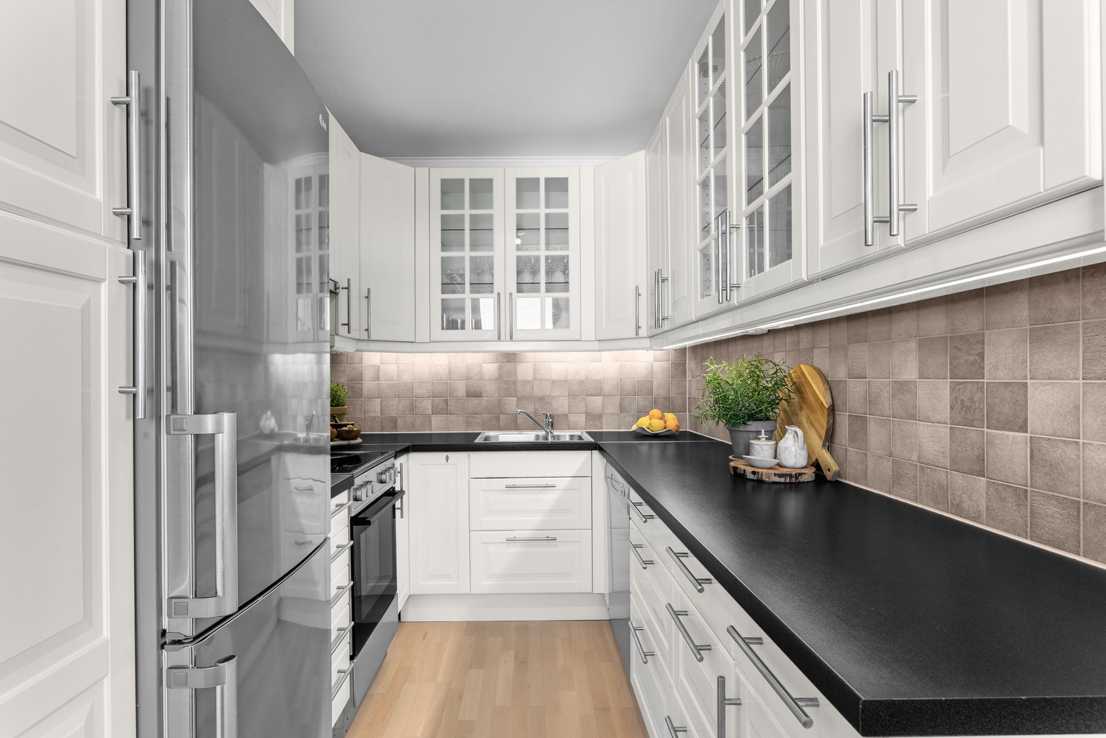Kjøkkeninnredning med profilerte fronter, noen vitrinefronter, og laminat benkeplate med nedfelt kum i rustfritt stål. Galleribilde