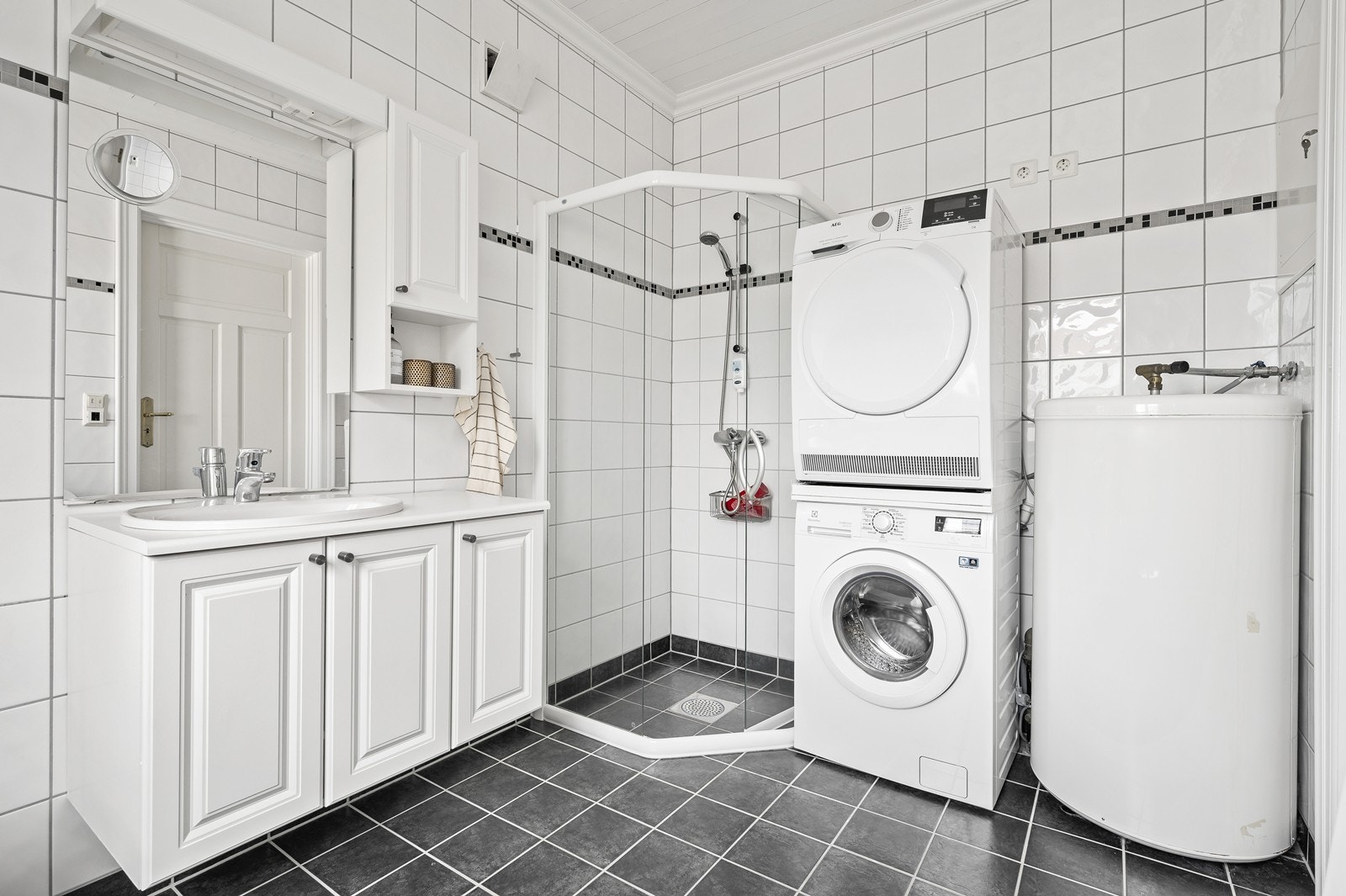 Badet i 1. etg. er flislagt med varmekabler i gulv. Rommet inneholder servant med over- og underskap, badekar, wc, opplegg til vaskemaskin og dusjhjørne. Galleribilde