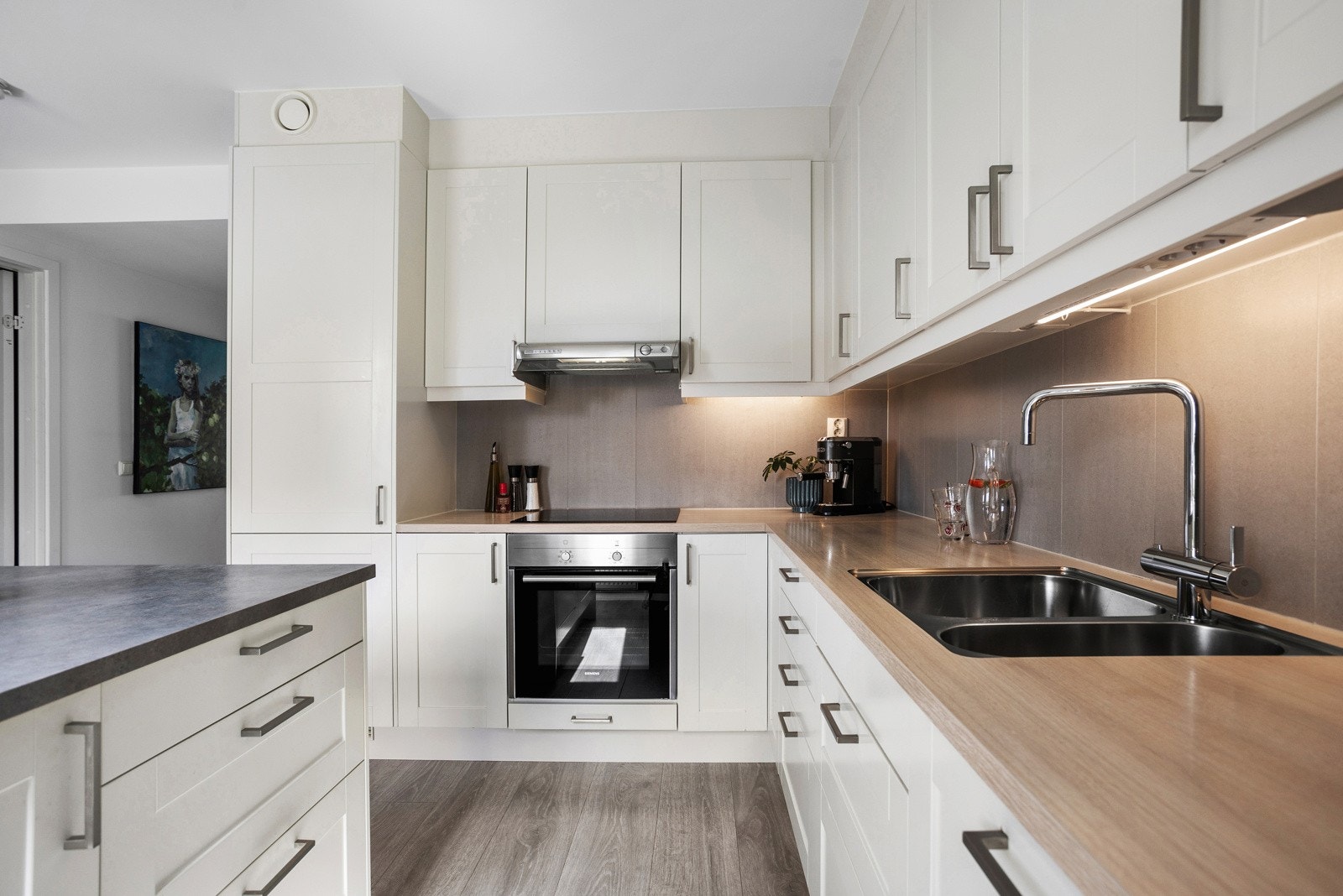 Her har du hvite profilerte fronter, laminat benkeplater og pene fliser mellom benk og skap. Galleribilde