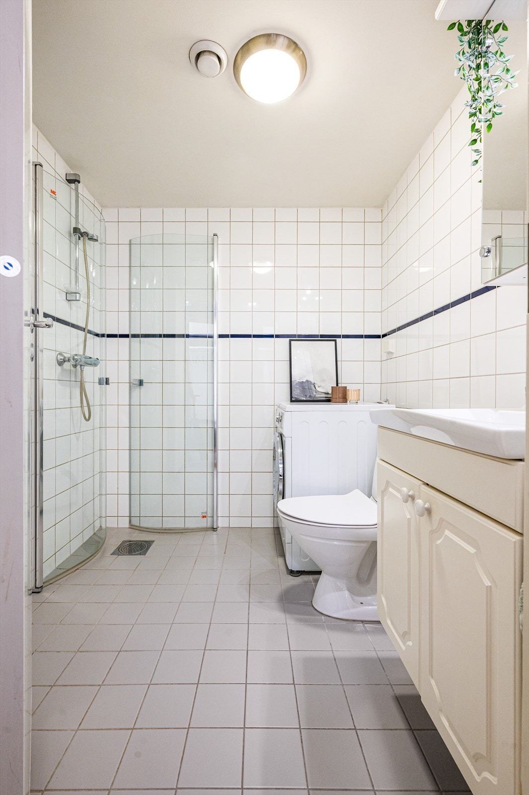 Badet er innredet med dusjhjørne med glassvegger, veggmontert speilskap med belysning, heldekkende servant med underskap, og gulvstående toalett. Galleribilde