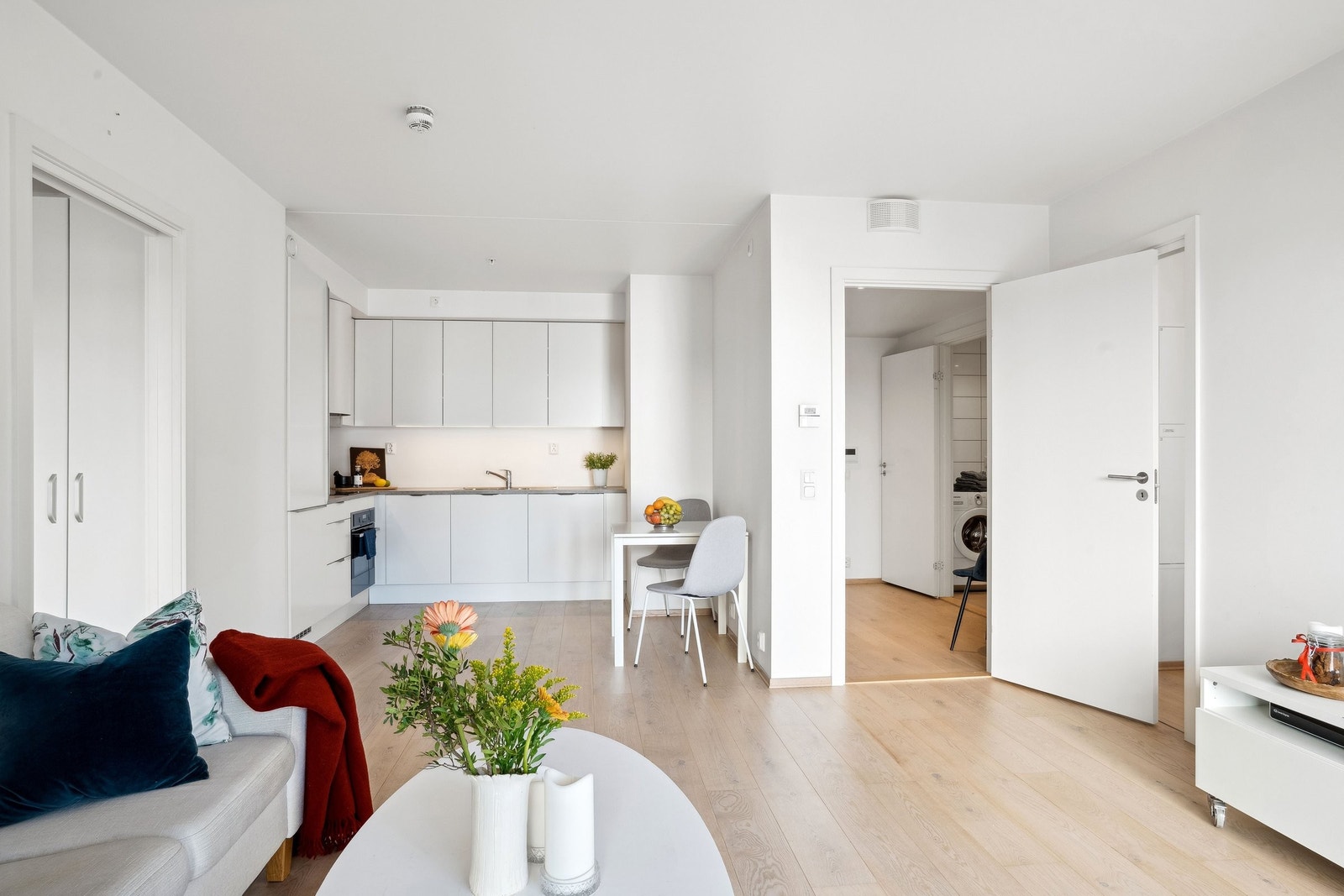 Lys stue med åpen kjøkkenløsning – gjennomgående parkett og stilrent kjøkken med hvite fronter og laminat benk. Galleribilde