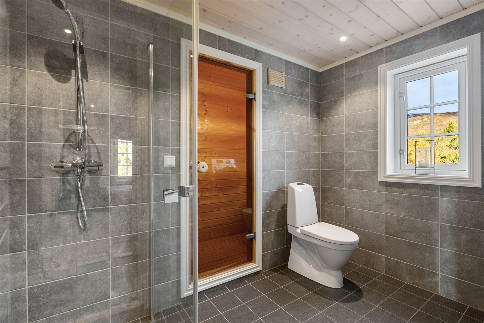 Delikat flislagt bad i tidløse farger med behagelig gulvvarme og badstue Galleribilde