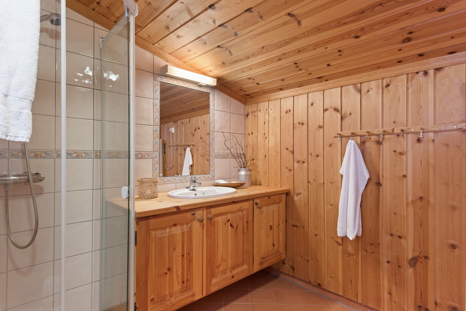 Badet er et funksjonelt baderom som inneholder vegger kledd med trepanel og fliser. Galleribilde