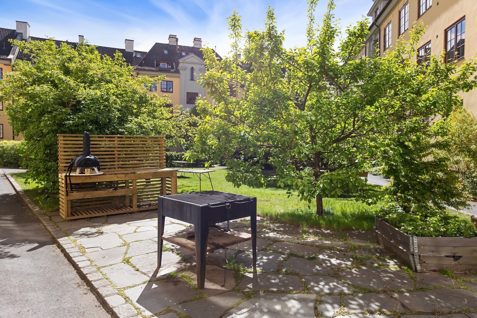 Grillplass med pizzaovn, bugnende trær og beplantning - et sjarmerende uterom i klassisk engelsk hageby-stil. Galleribilde