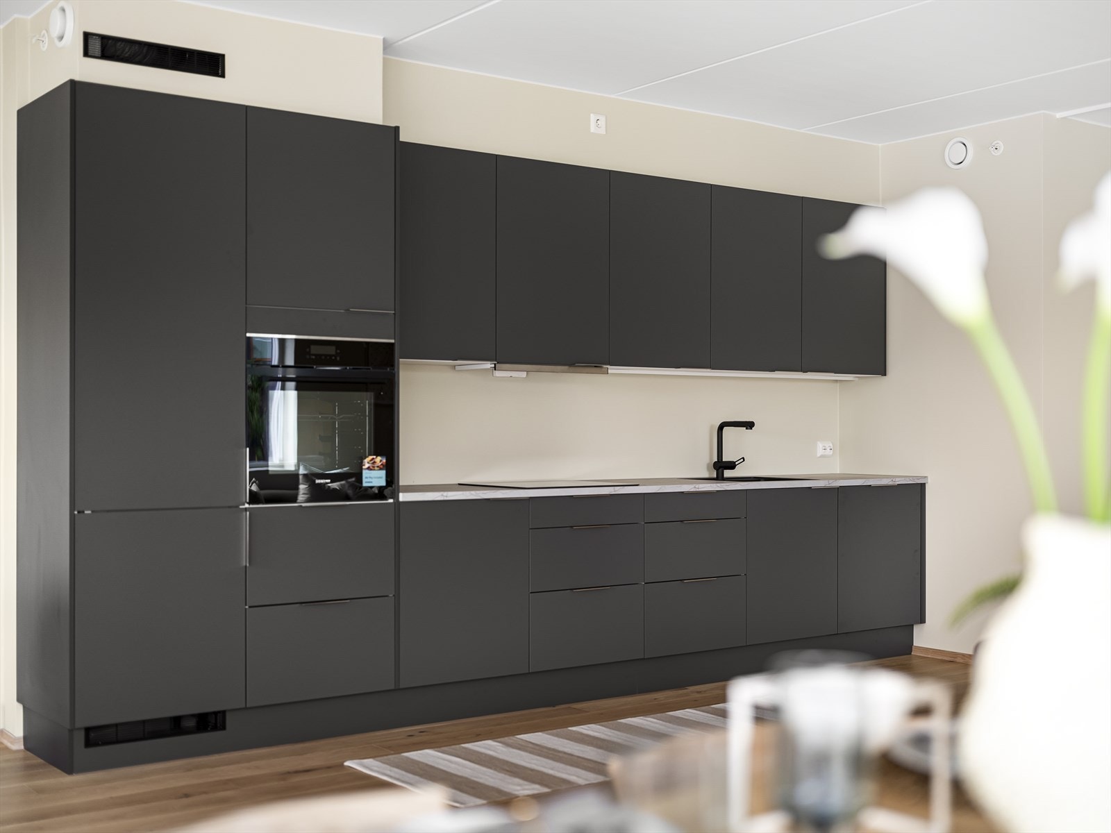 Integrerte hvitevarer som induksjonstopp, oppvaskmaskin, kjøleskap og stekeovn plassert i ståhøyde. Galleribilde