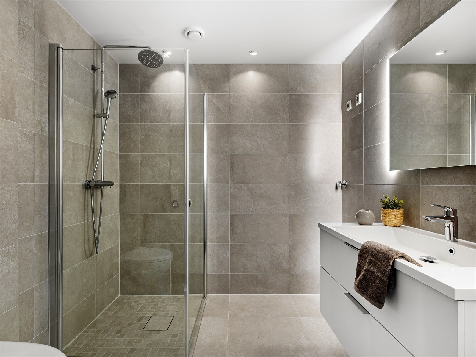 Badet er delikat med fliser på vegger og gulv og downlights i himling. Badet er innredet med vask i seksjon, speil med belysning, veggehengt toalett, foldbare dusjdører i glass og opplegg for vaskemaskin. Galleribilde