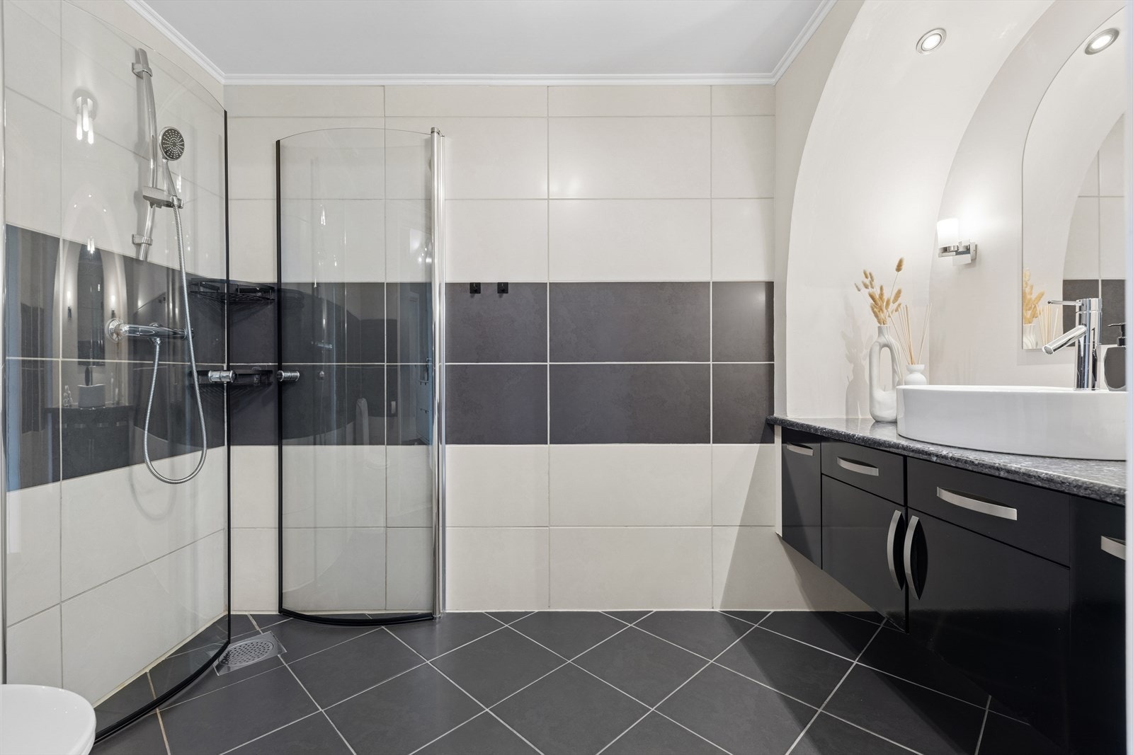 Badet har flislagt gulv og er innredet med mørk, høyglanset baderomsinnredning, solid servant og spotlights i taket. Galleribilde