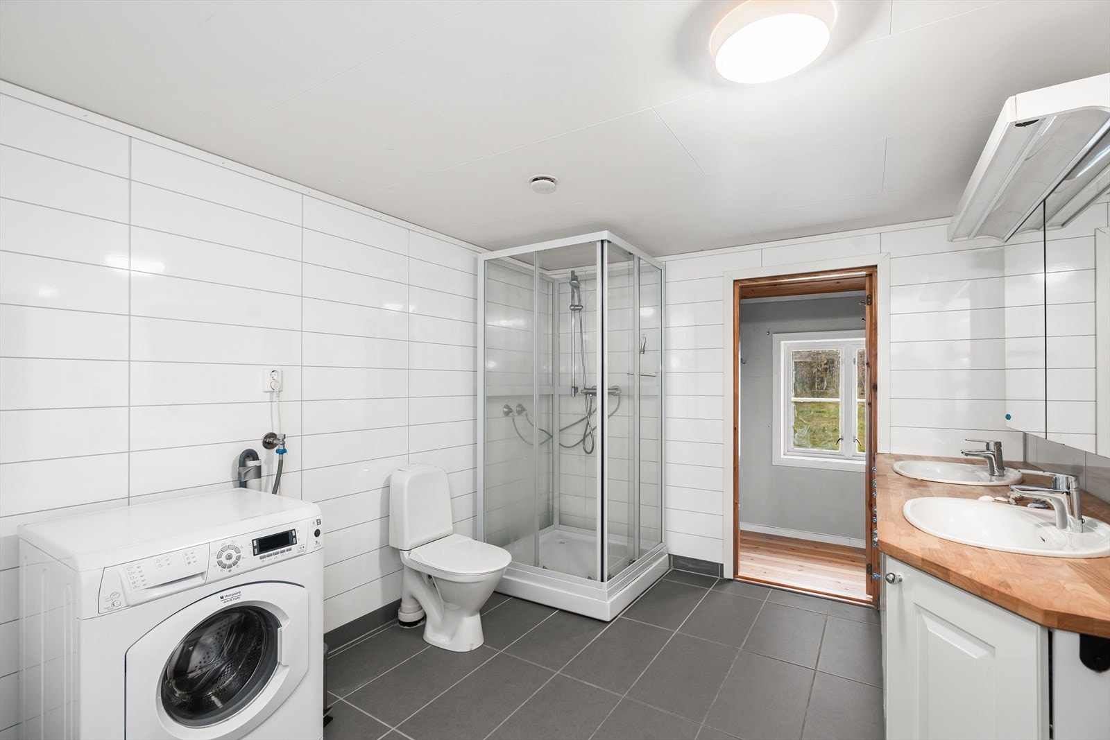 Det er flis på gulv og våtromsplater på vegger. Badet er utstyrt badekar, dusjkabinett, naturlig avtrekk, opplegg for vaskemaskin, servant, servantskap og wc. Galleribilde