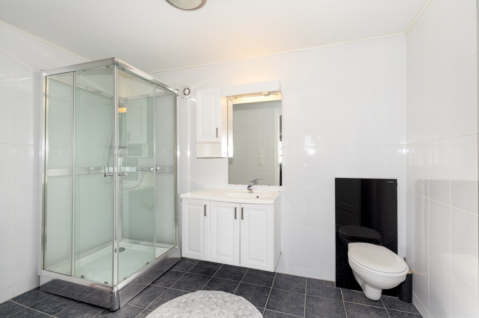 Flislagt bad innredet med servantskap, vegghengt toalett og dusjkabinett. Dusjkabinettet har knust glass, og må byttes. Galleribilde