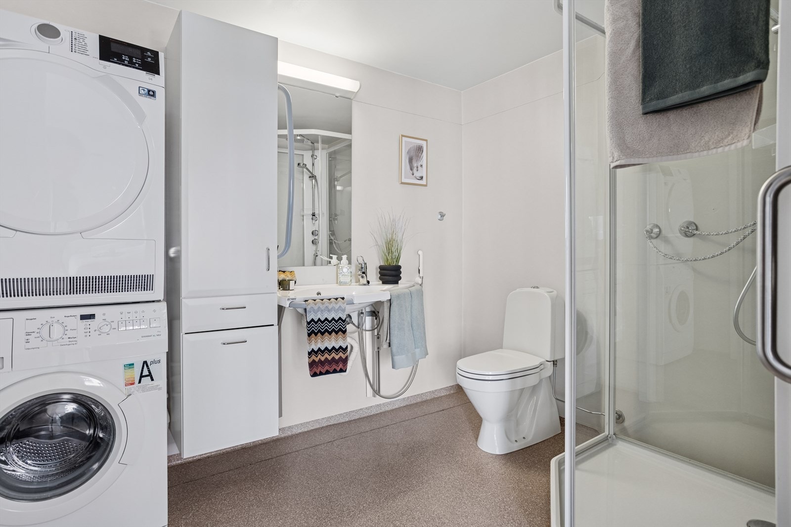 Badet er også romslig, med sine 5,6 m². Her er det lukket dusjkabinett, toalett, servant og veggskap. Det er opplegg til vaskemaskin. Galleribilde