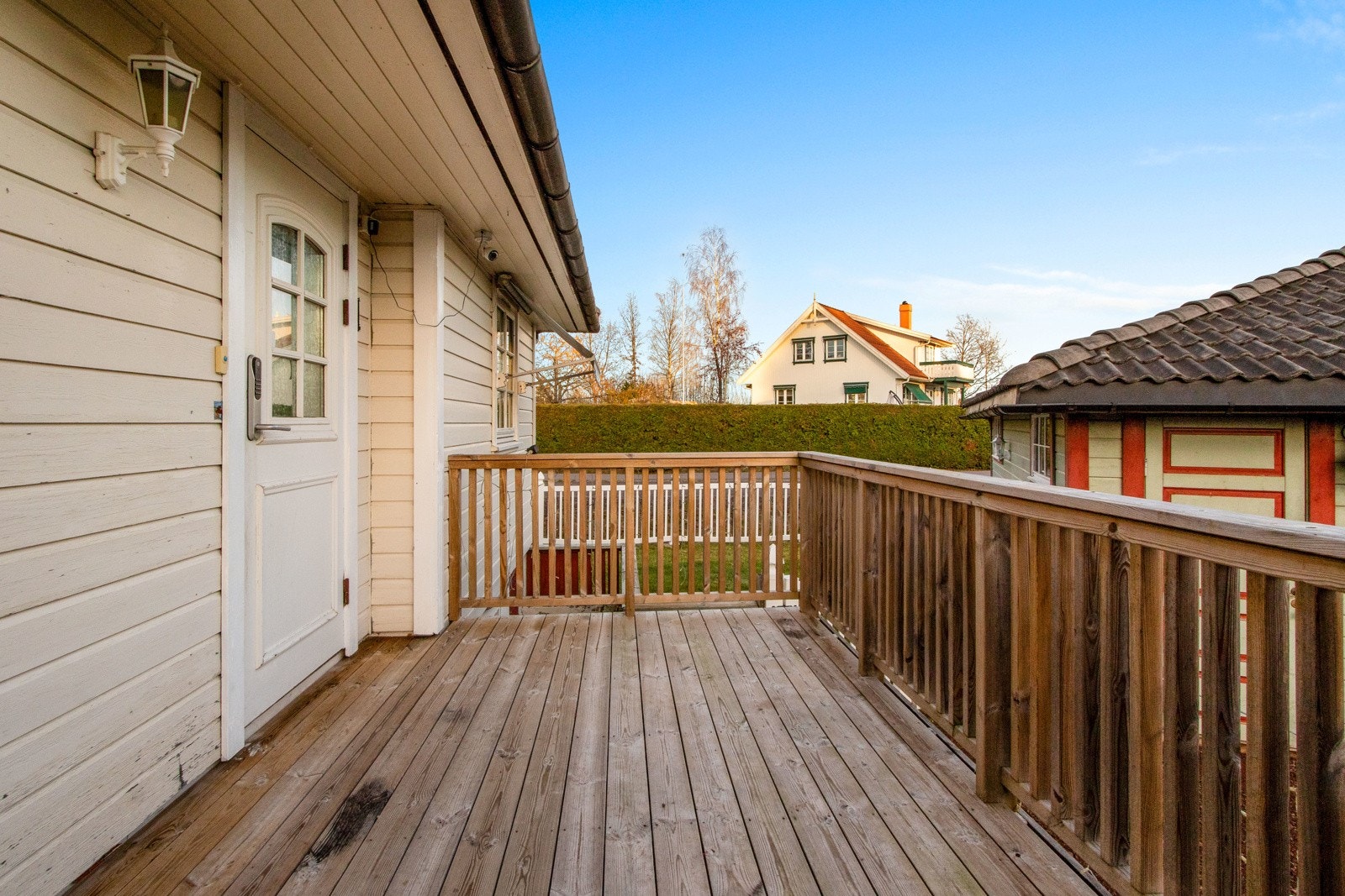 Eneboligen har et flott inngangsparti i første etasje med veranda, utebelysning montert på veggen og hvit, overbygd inngangsdør med glassfelt. Galleribilde