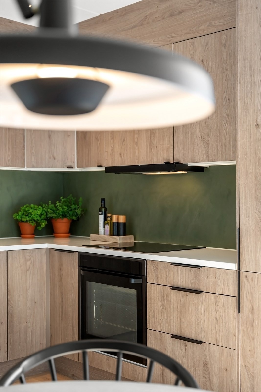 Kjøkkeninnredning med glatte fronter, mikrosement på vegg over benkeskap, belysning under overskap og benkeplate i komposittstein Galleribilde