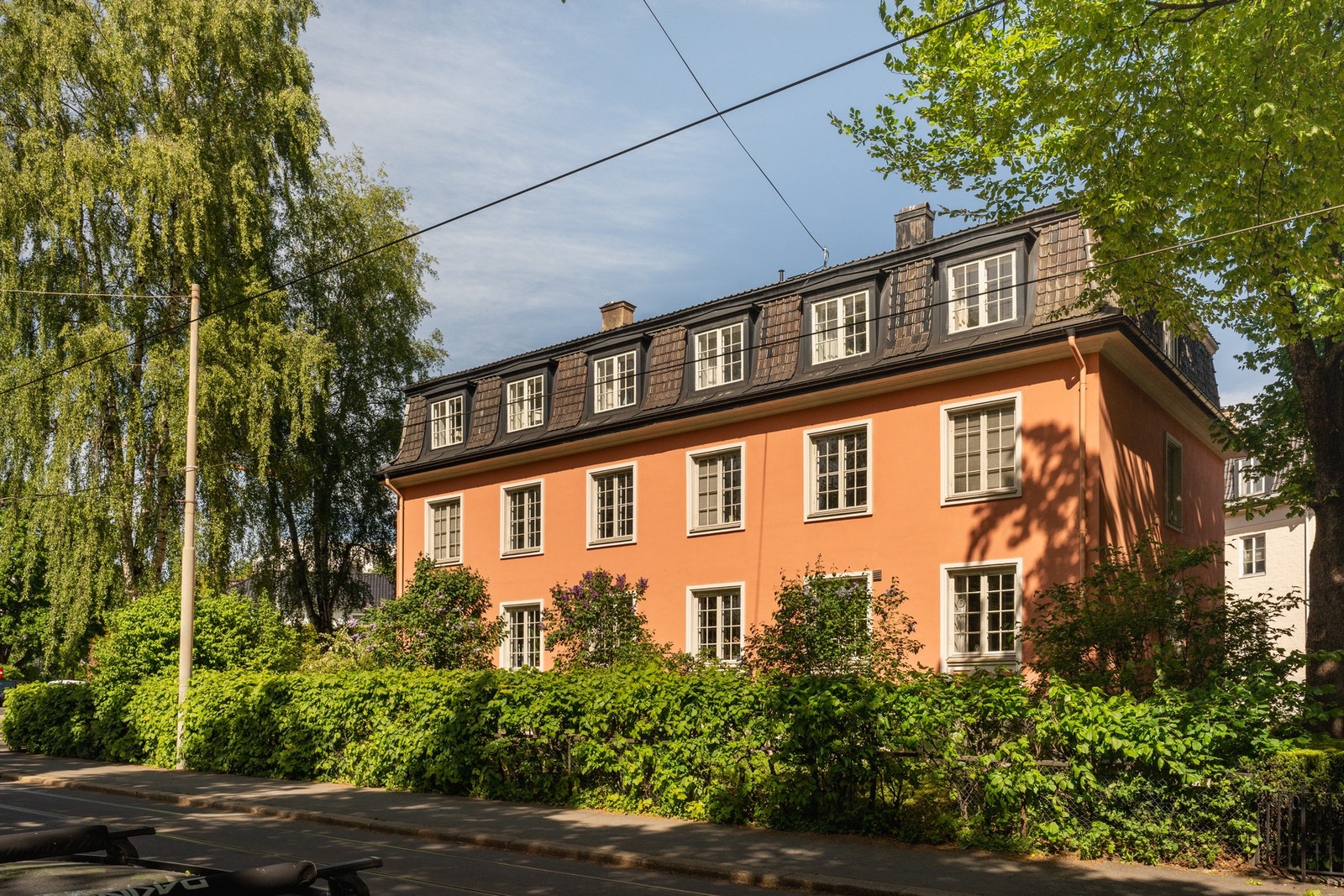 To ærverdige bjerker vokser på hver side av hovedinngangen. Bygget har mansardtak og store vinduer med små ruter. Galleribilde