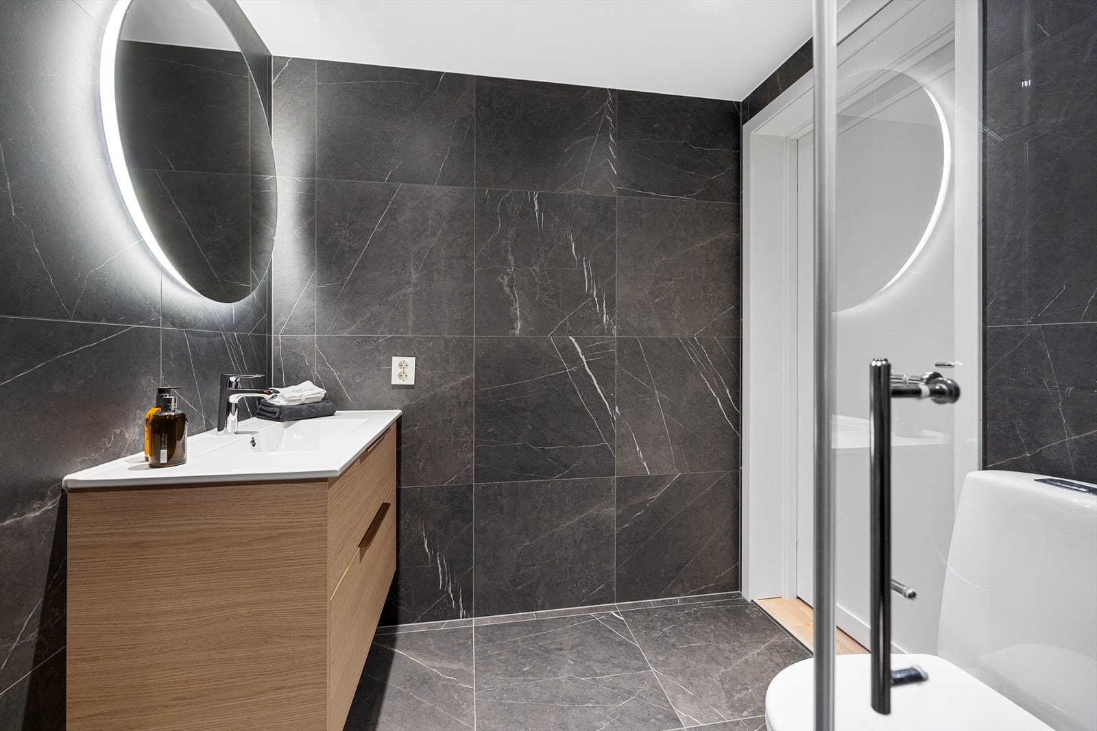 Badet er innredet med helstøpt servant i innredning med 2 skuffer. Speil med belysning. Toalett. Dusj med takdusj og hånddusj, samt innfellbare glassdører Galleribilde