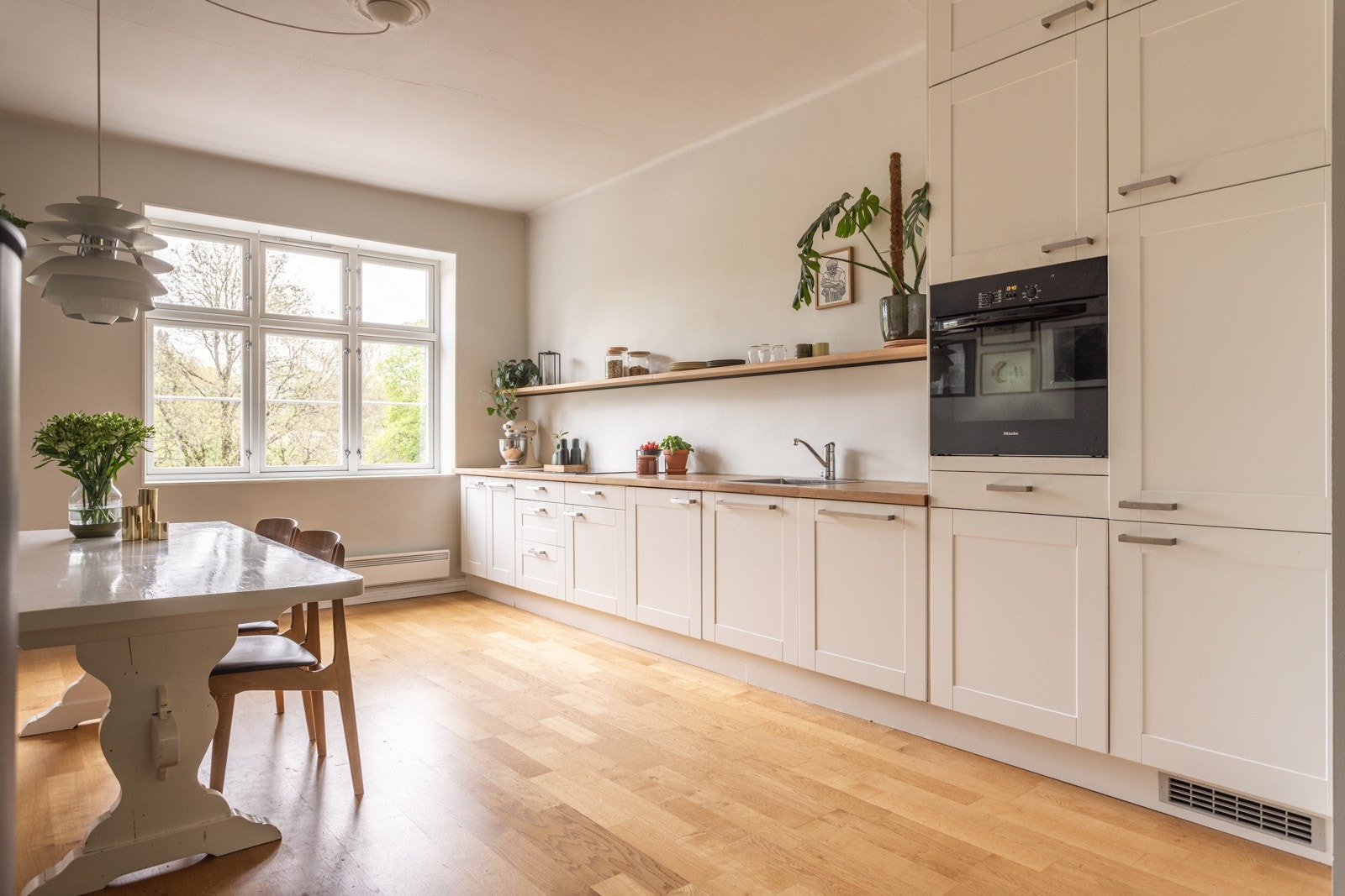 Delikat innredning med hvite profilerte fronter, integrerte hvitevarer, heltre benkeplate og flott overhylle i eik. Galleribilde