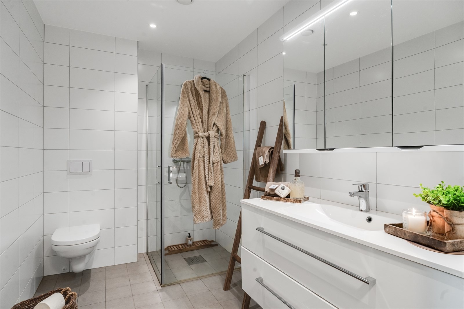 Pent helfliset baderom med dusj, baderomsseksjon, speilskap og vegghengt toalett Galleribilde