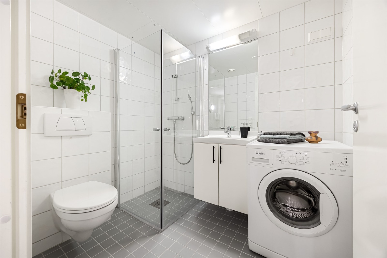 Flislagt pent bad med vegghengt toalett, dusjhjørne, servant med skap og vaskemaskin. Det er satt inn nye dusjdører og vaskemaskin medfølger. Galleribilde